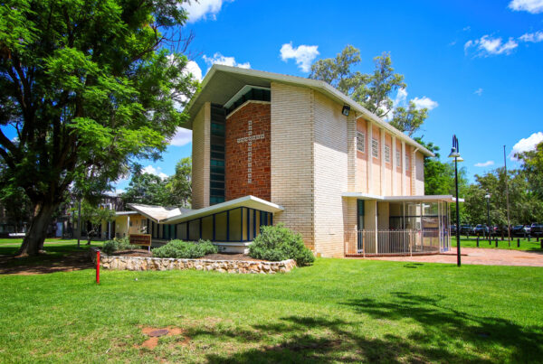A modern-looking church made of tan-coloured bricks, with a red feature wall and cross.