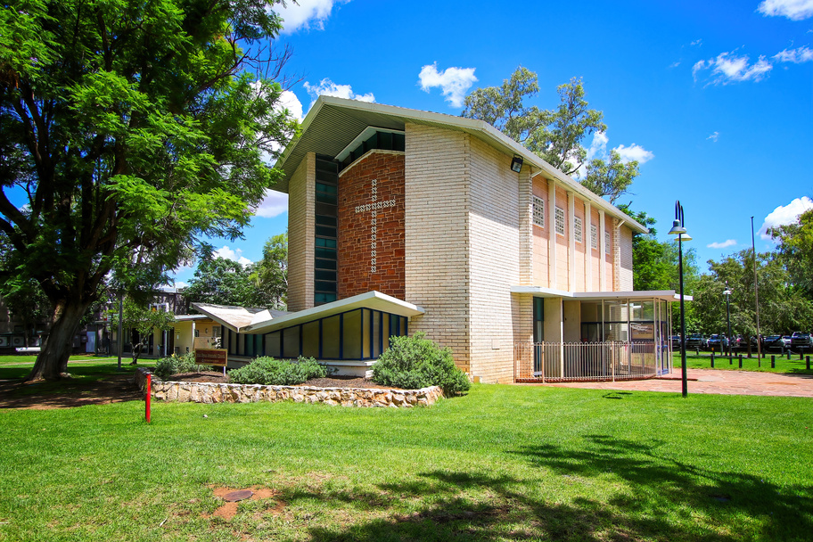A modern-looking church made of tan-coloured bricks, with a red feature wall and cross.